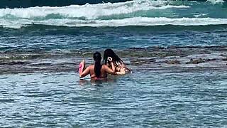Two pretty brunettes kiss on the public beach at enseada dos corais