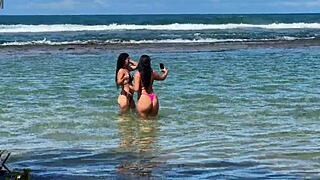 Two pretty brunettes kiss on the public beach at enseada dos corais