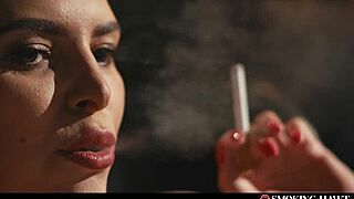 A brunette woman in lingerie smokes a cigarette while admiring her nails