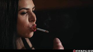 A brunette woman in lingerie smokes a cigarette while admiring her nails